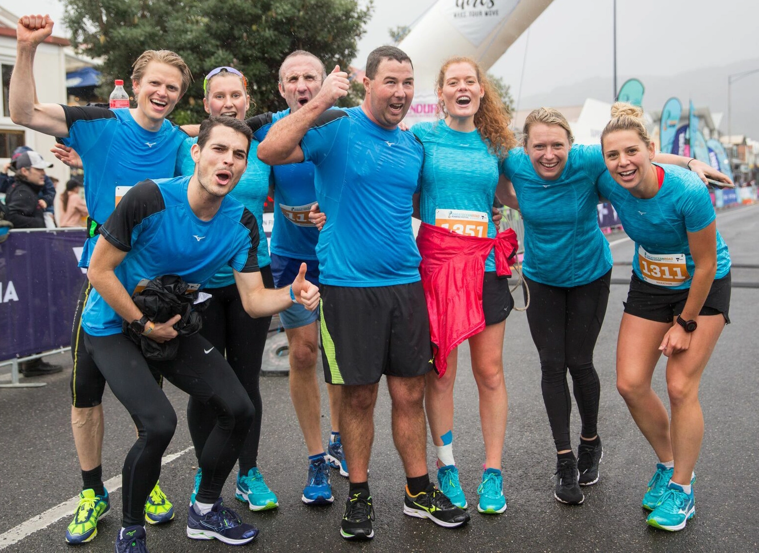 Nathan surrounded by 7 people all wearing blue running tops and celebrating at the finish line of an event